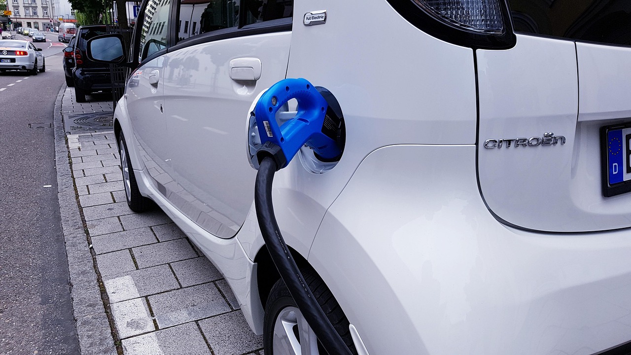 White electric car charging at the kerb with a blue plug on a concrete footpath